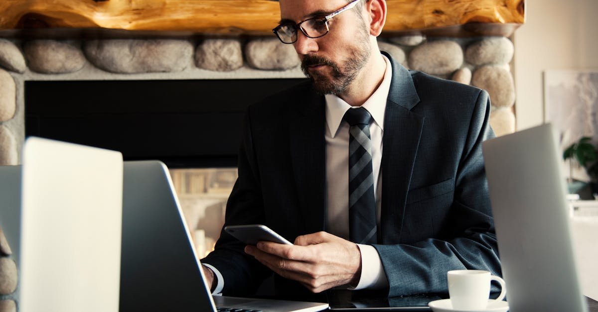 Businessman in formal attire working on a laptop and smartphone at an indoor office desk.